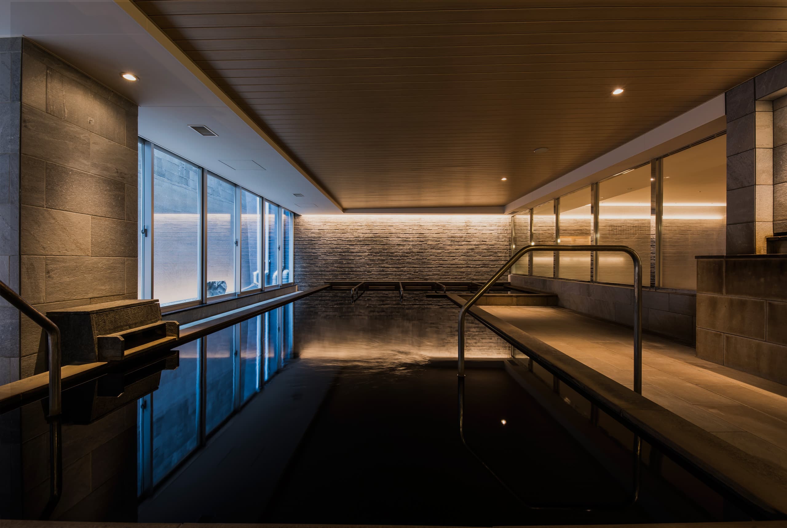 Traditional onsen bath at Aqua Sports & Spa Tokyo — dim-lit indoor stone-clad hot bath