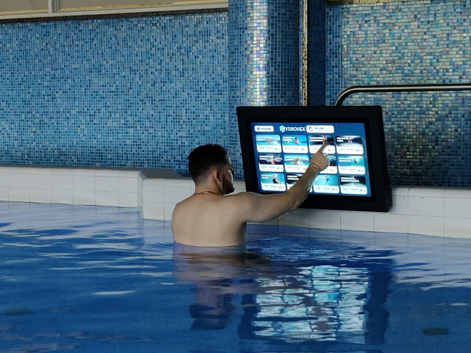 En besökare väljer sitt pass på en vattentät touchskärm vid poolkanten